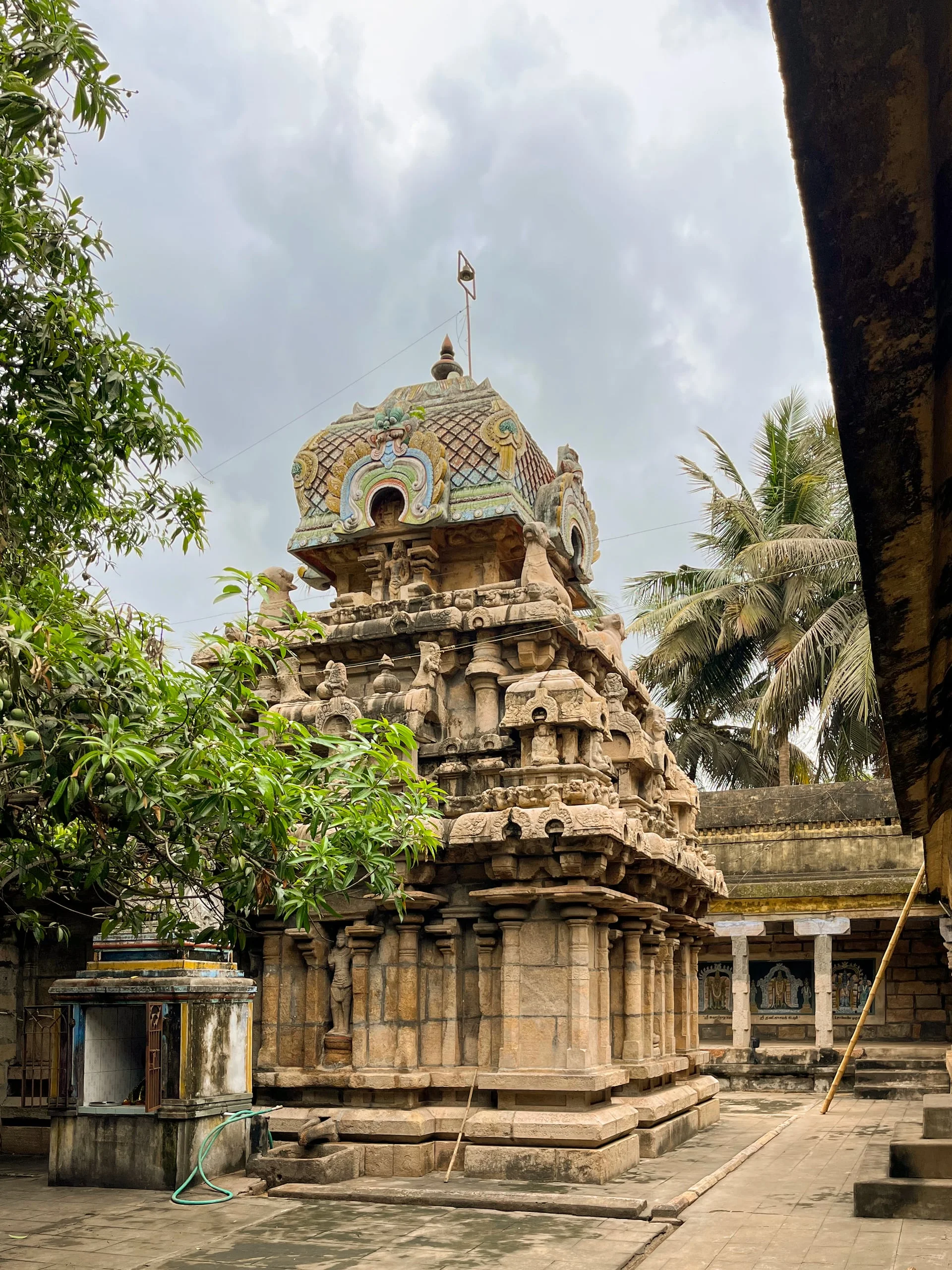 Classical stone shrine in temple courtyard with granite base and sculpted stucco superstructure under clouds.
